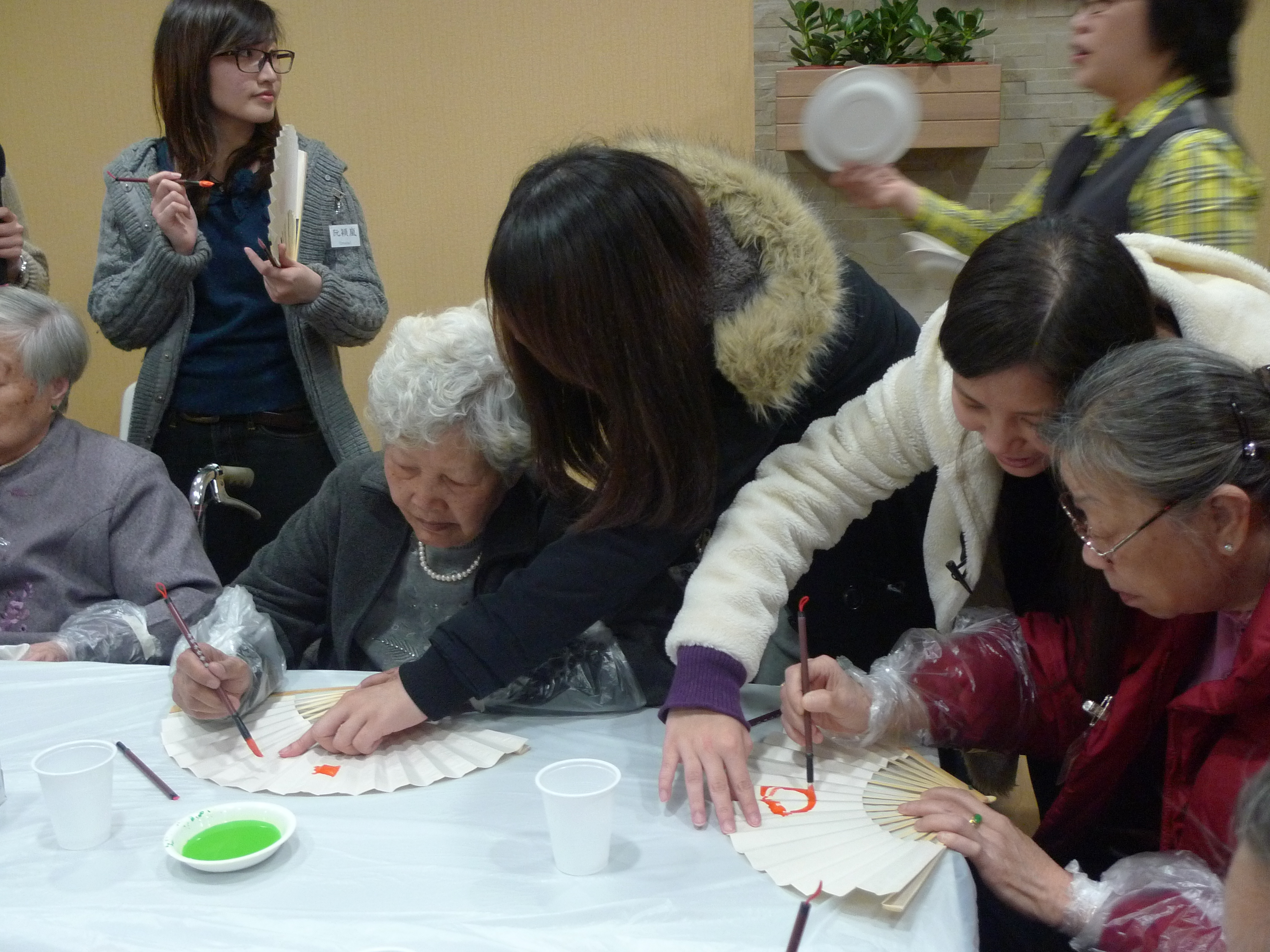 Volunteers helping the elders paint the paper fans.