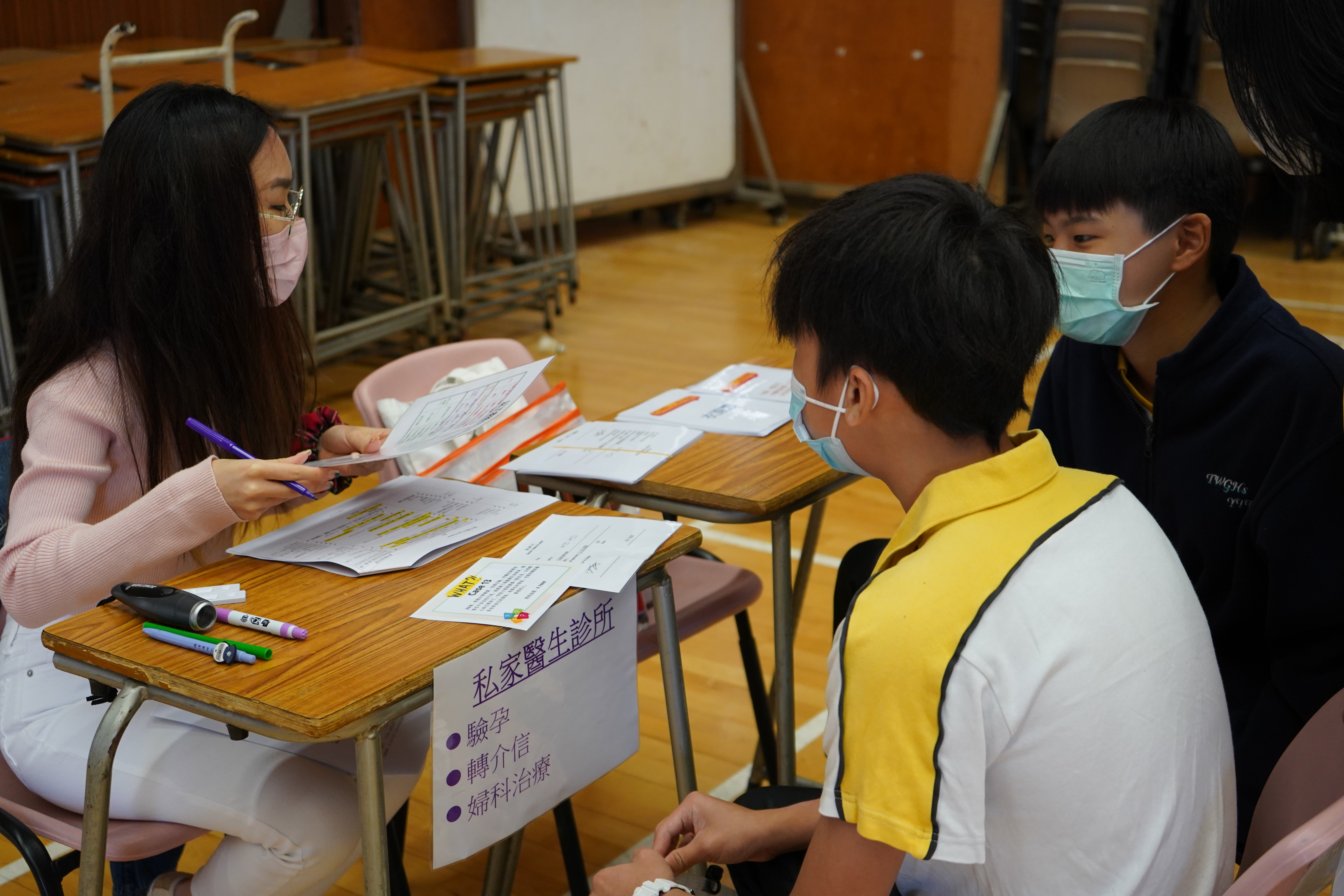 Two secondary students are sitting in front of a volunteer who pretended as a doctor