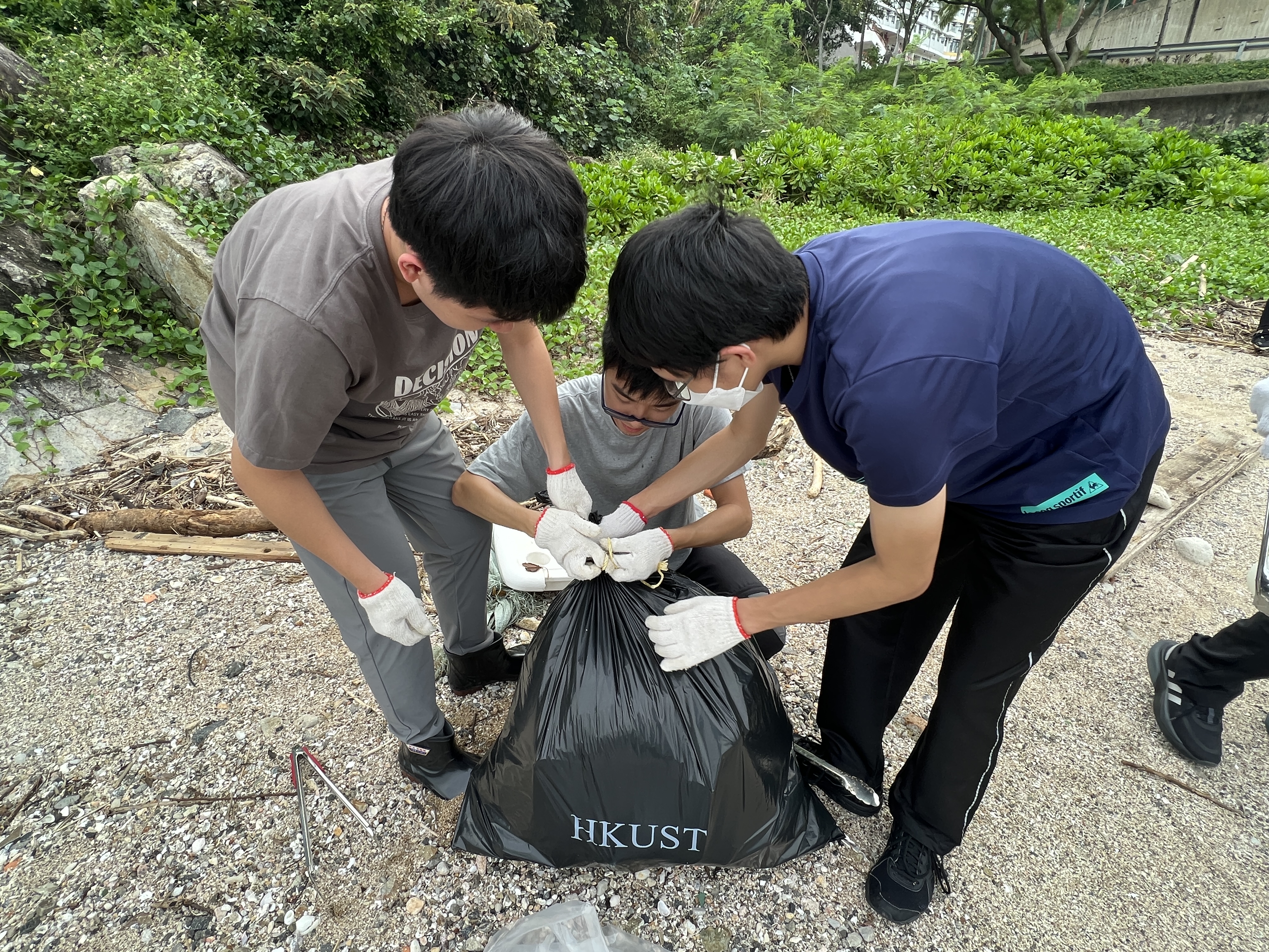 Volunteers working together to tie up a bag full of litter.