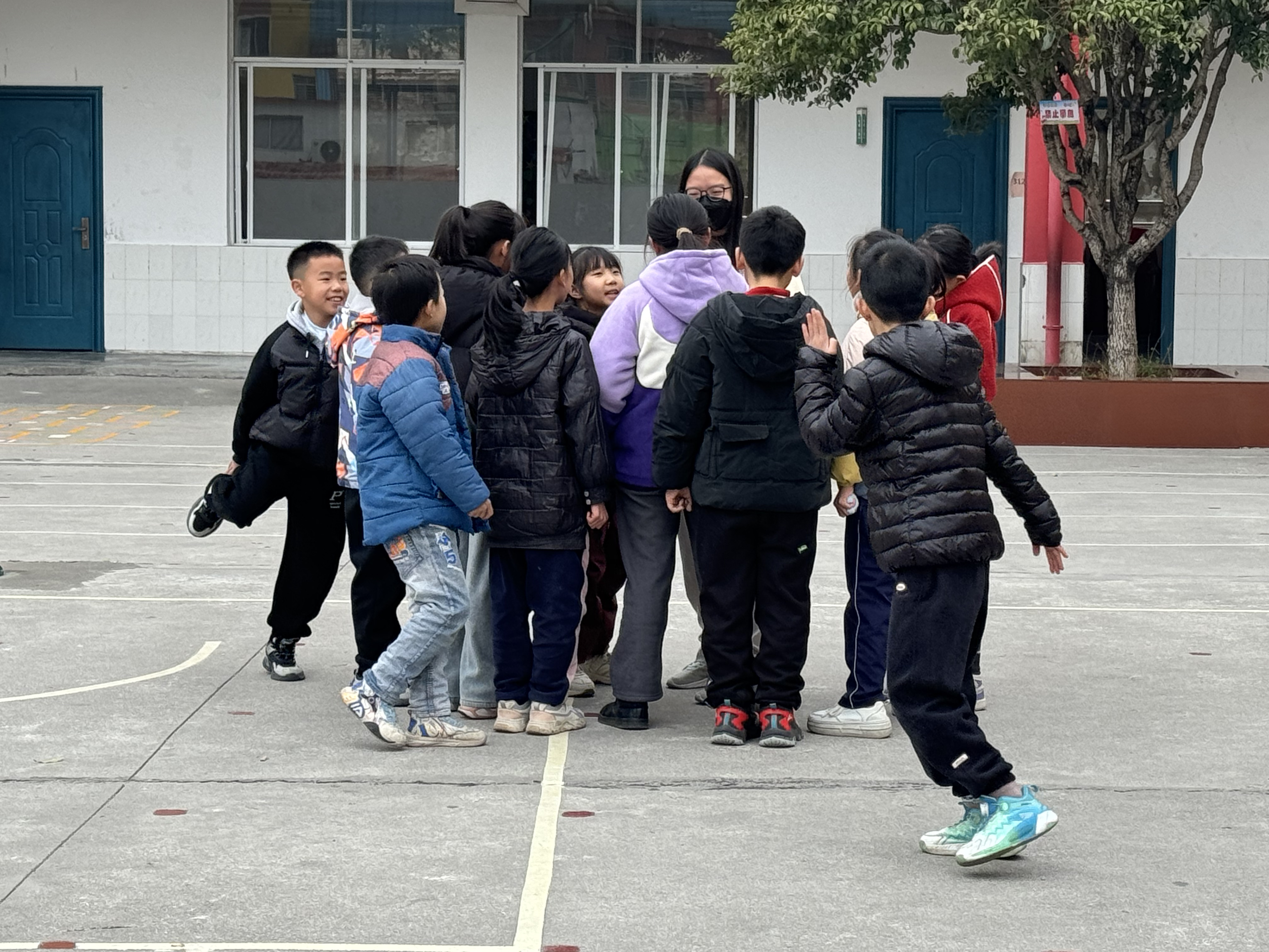 Students gathering around a volunteer during break time, inviting them to join in their games