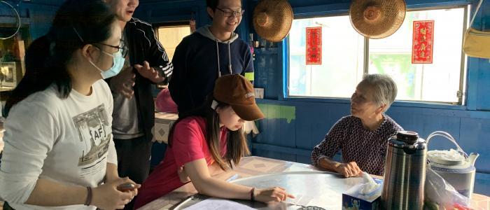 students chatting with a older woman in a stilt house