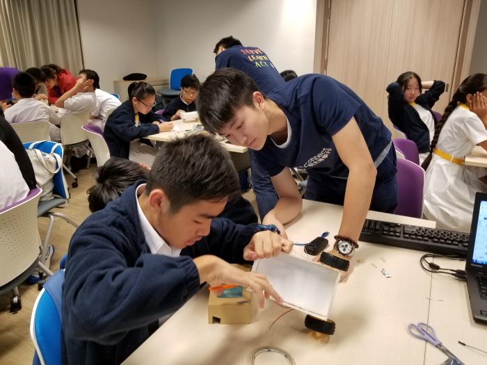 Volunteers help a student finish the STEM workshop.