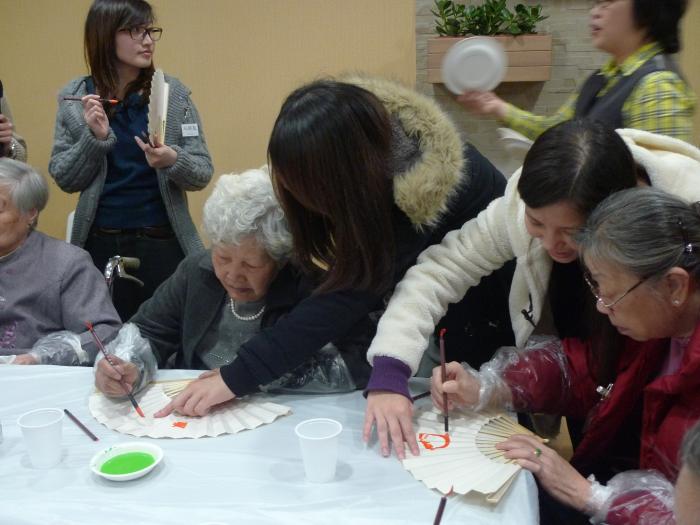 Volunteers helping the elders paint the paper fans.