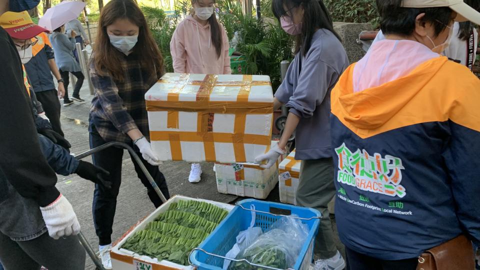 Volunteers are moving boxes of surplus vegetables to the trolley.