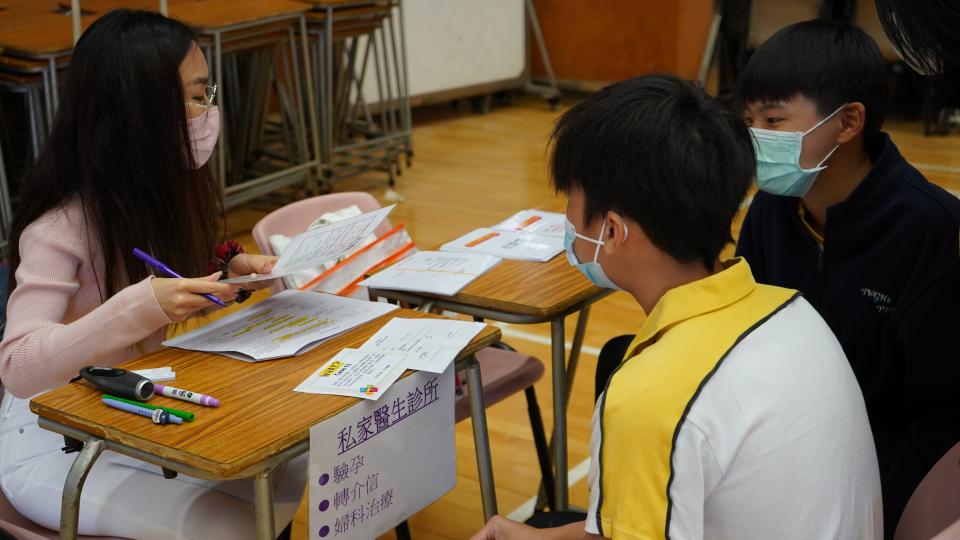 Two secondary students are sitting in front of a volunteer who pretended as a doctor
