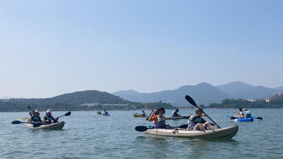 participants rowing kayaks in the sea under a blue sky